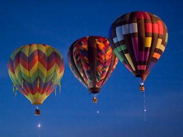 3 hot air balloons hovering in the air at dawn