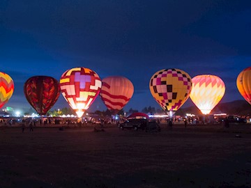 Seven glowing hot air balloons lined up at dawn