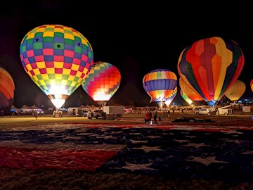 Multiple hot air balloons lit up at night tethered to the ground